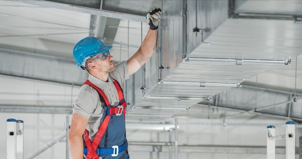 A male worker in safety gear installs air ducts.