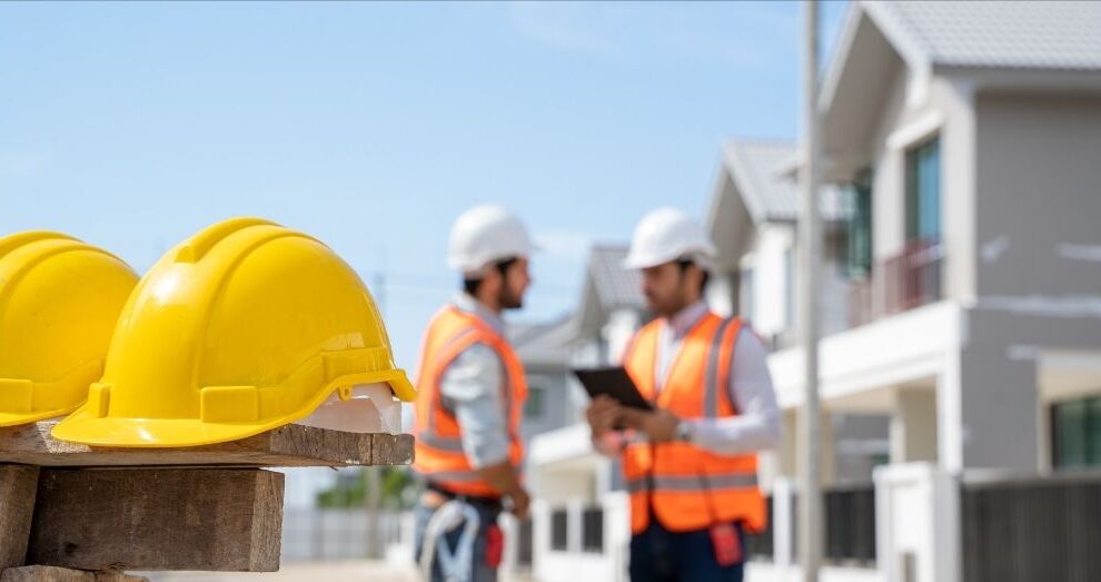 Two yellow hard hats with contractors in the background.