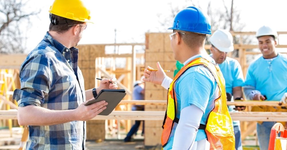 Two construction workers discuss plans using a tablet.