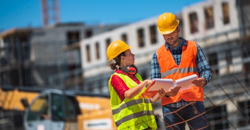 Two engineers review documents on a sunny construction site.
