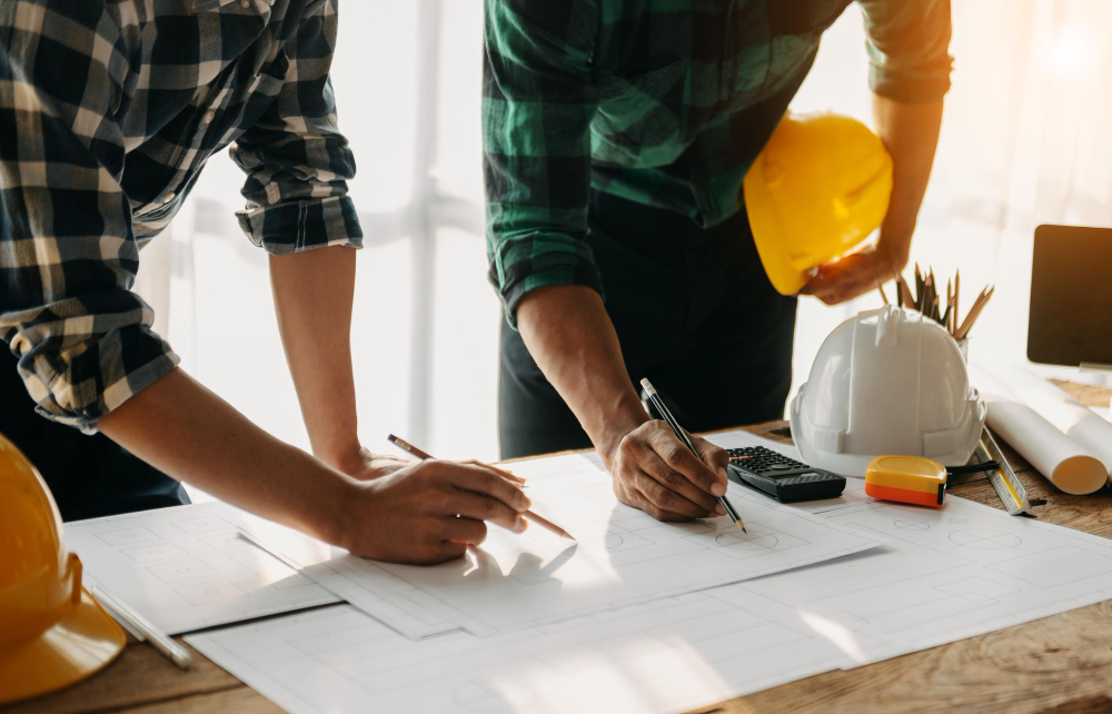 Construction contractors reviewing and marking building blueprints during a project planning phase with safety hard hats nearby.
